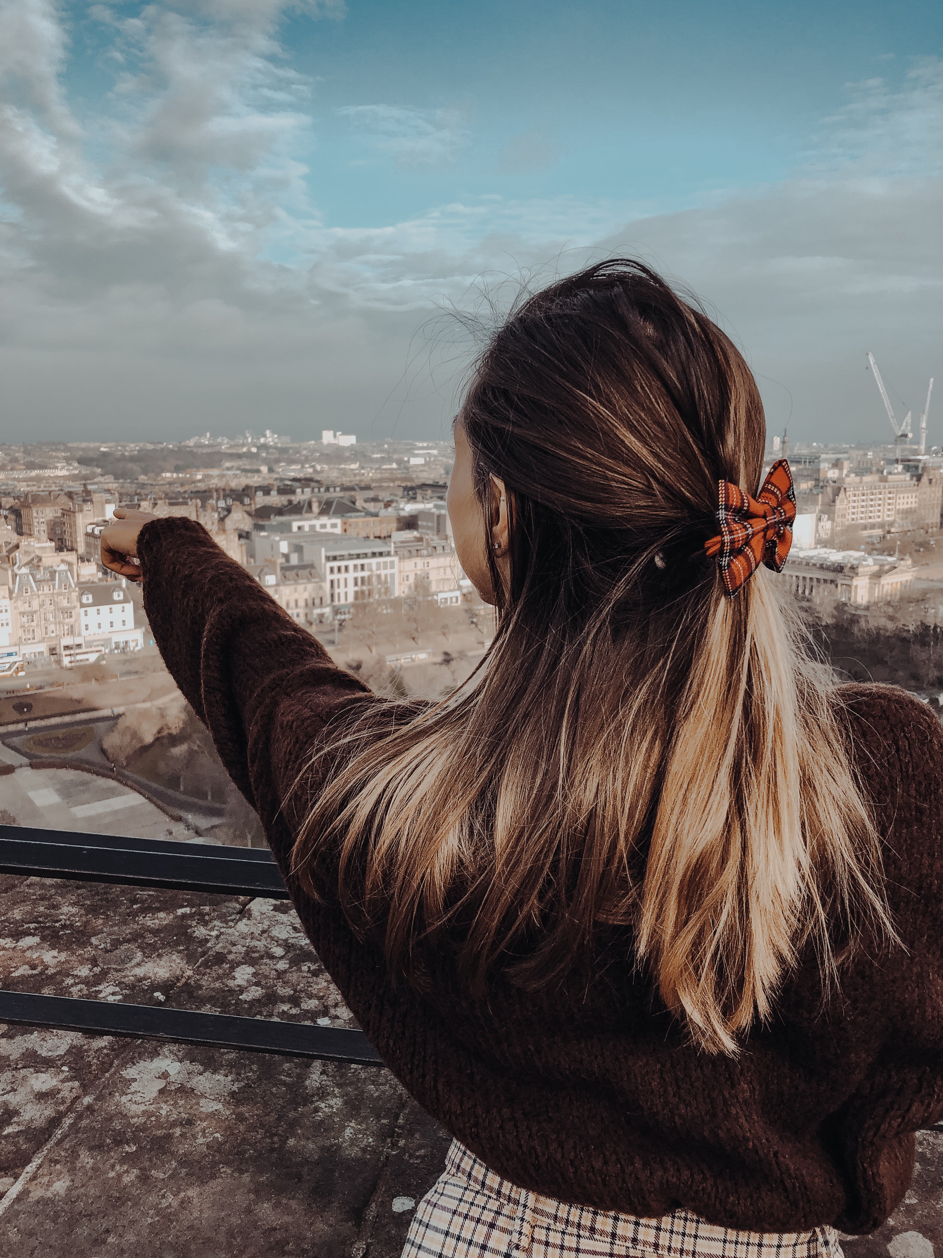 pointing to princes street from edinburgh castle girl wearing skirt jumper and tartan bow