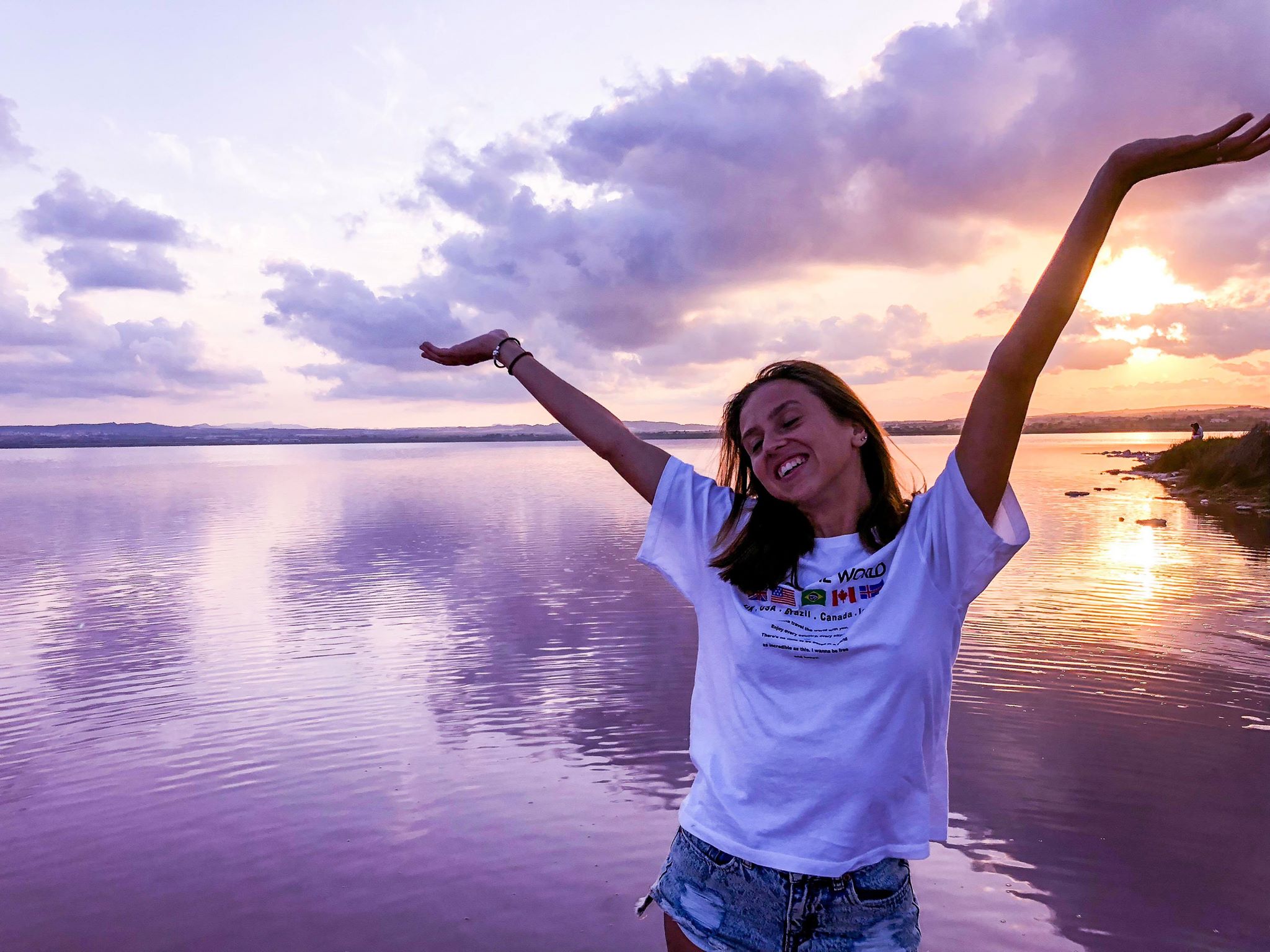 arms up smiling with pink water and sunset