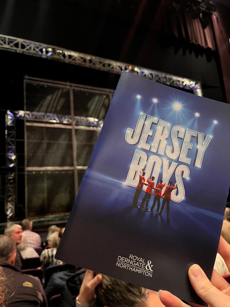 Jersey Boys programme held in front of the cage stage in the Royal and Derngate Northampton text says Jersey Boys and Derngate Northampton